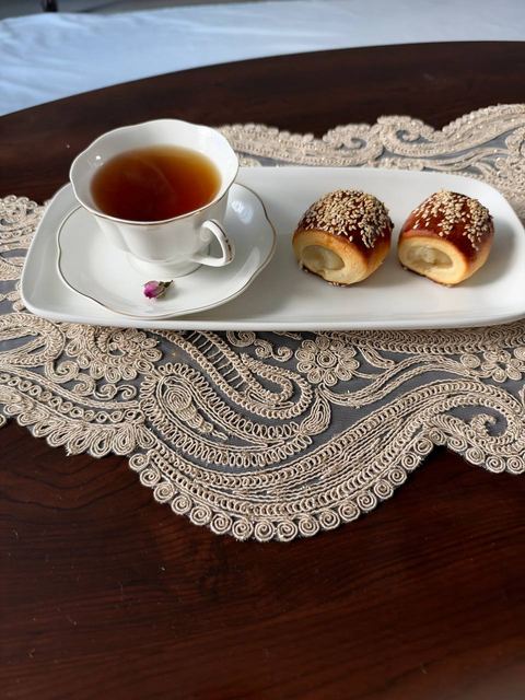 Two sesame-topped filled buns and a cup of tea on a white platter over a lace placemat