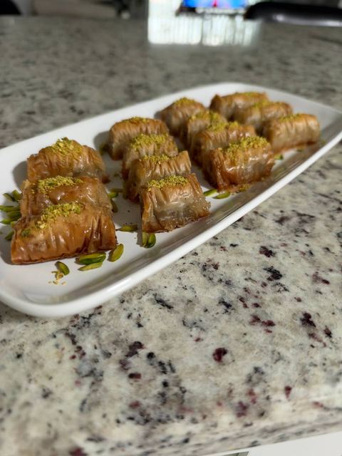 Baklava rolls sprinkled with pistachio on a white platter on a granite counter